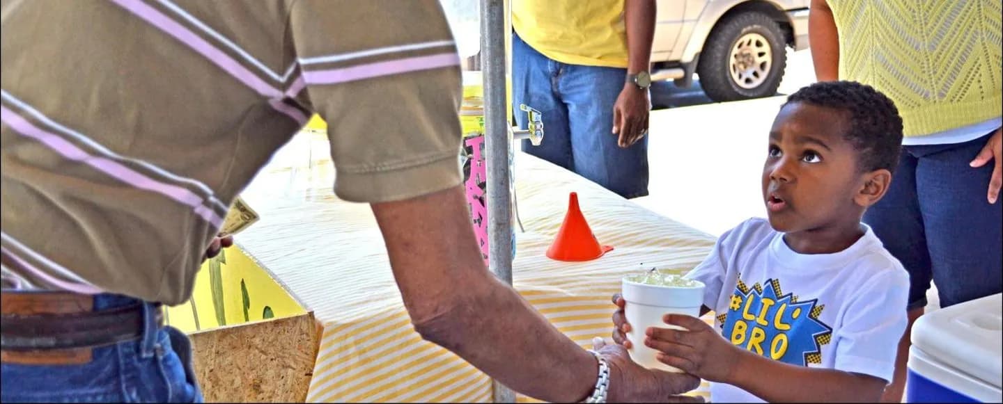 A boy proudly standing at his lemonade stand