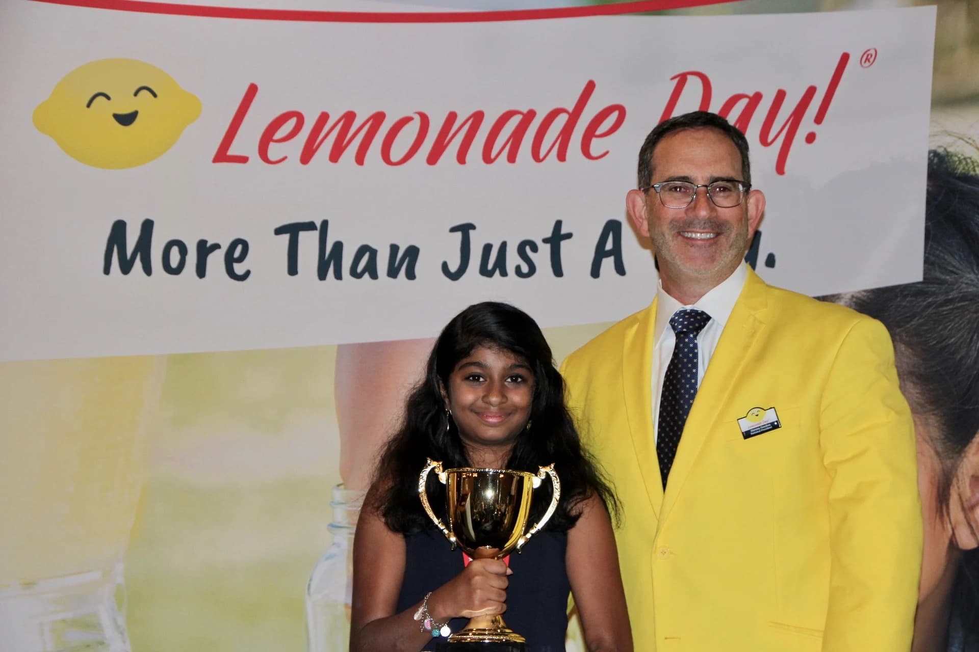 A girl holding her trophy beside a Lemonade Day board member