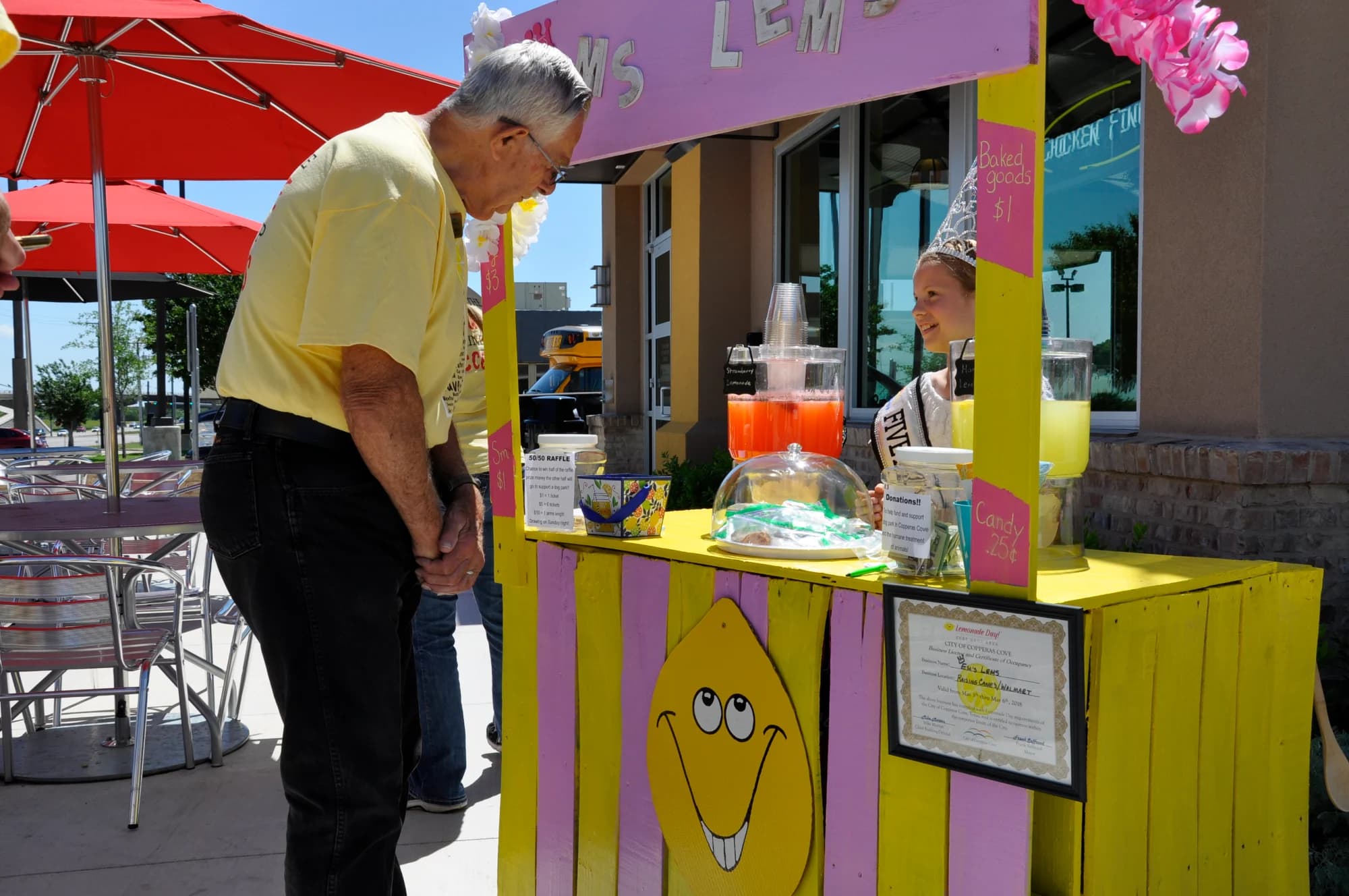 A grandfather buying lemonade from a girl at her purple and yellow stand