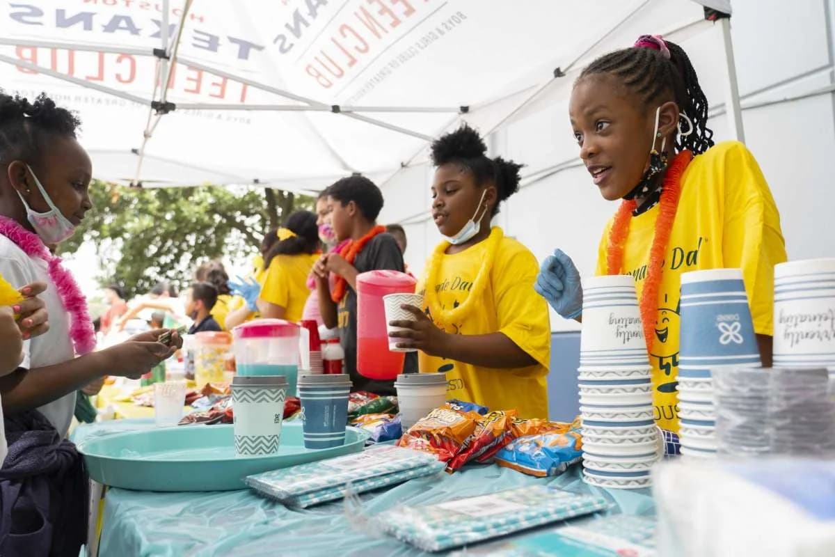 Kids in yellow shirts serving lemonade under a tent