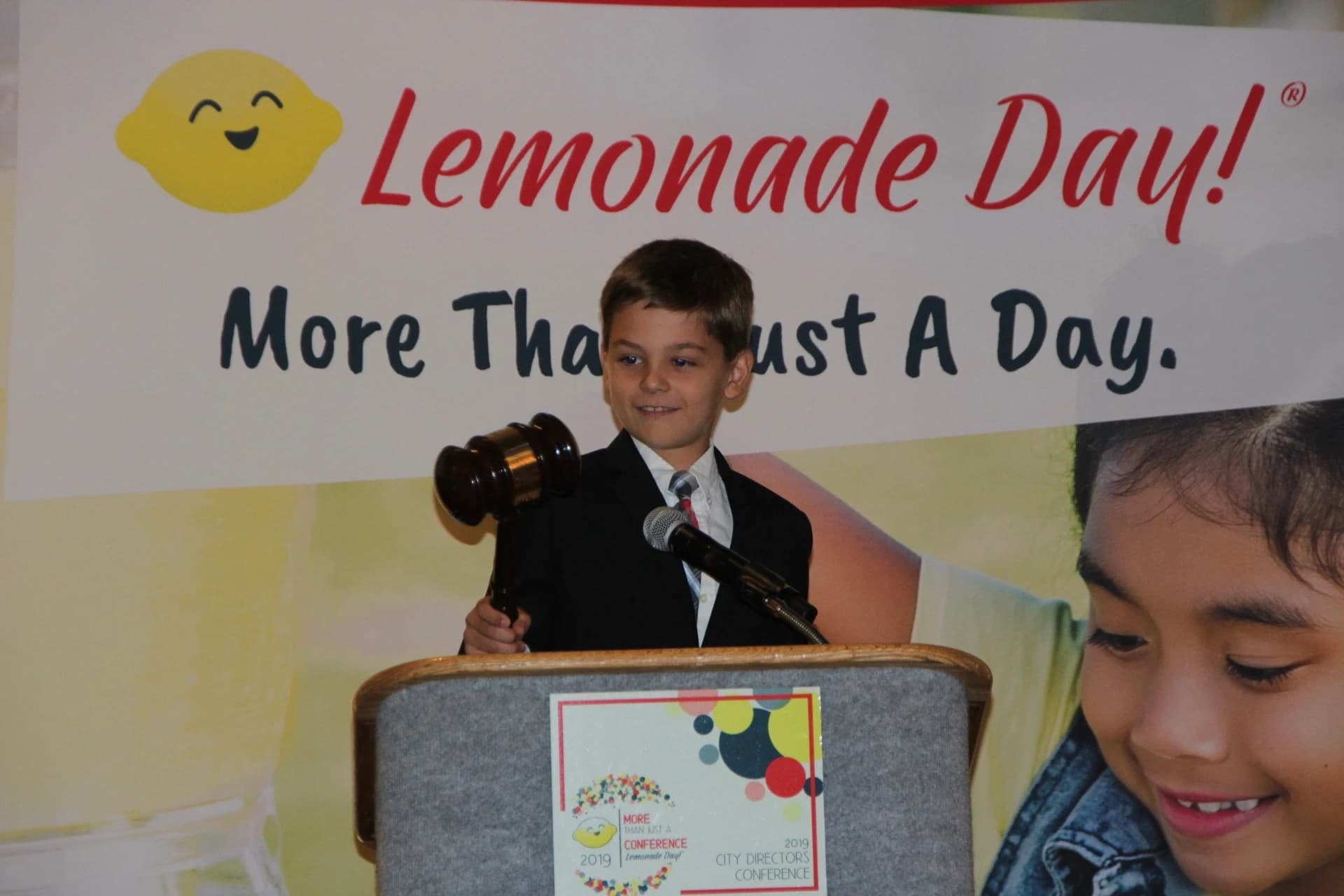 A boy speaking at the podium in front of the More Than Just A Day banner