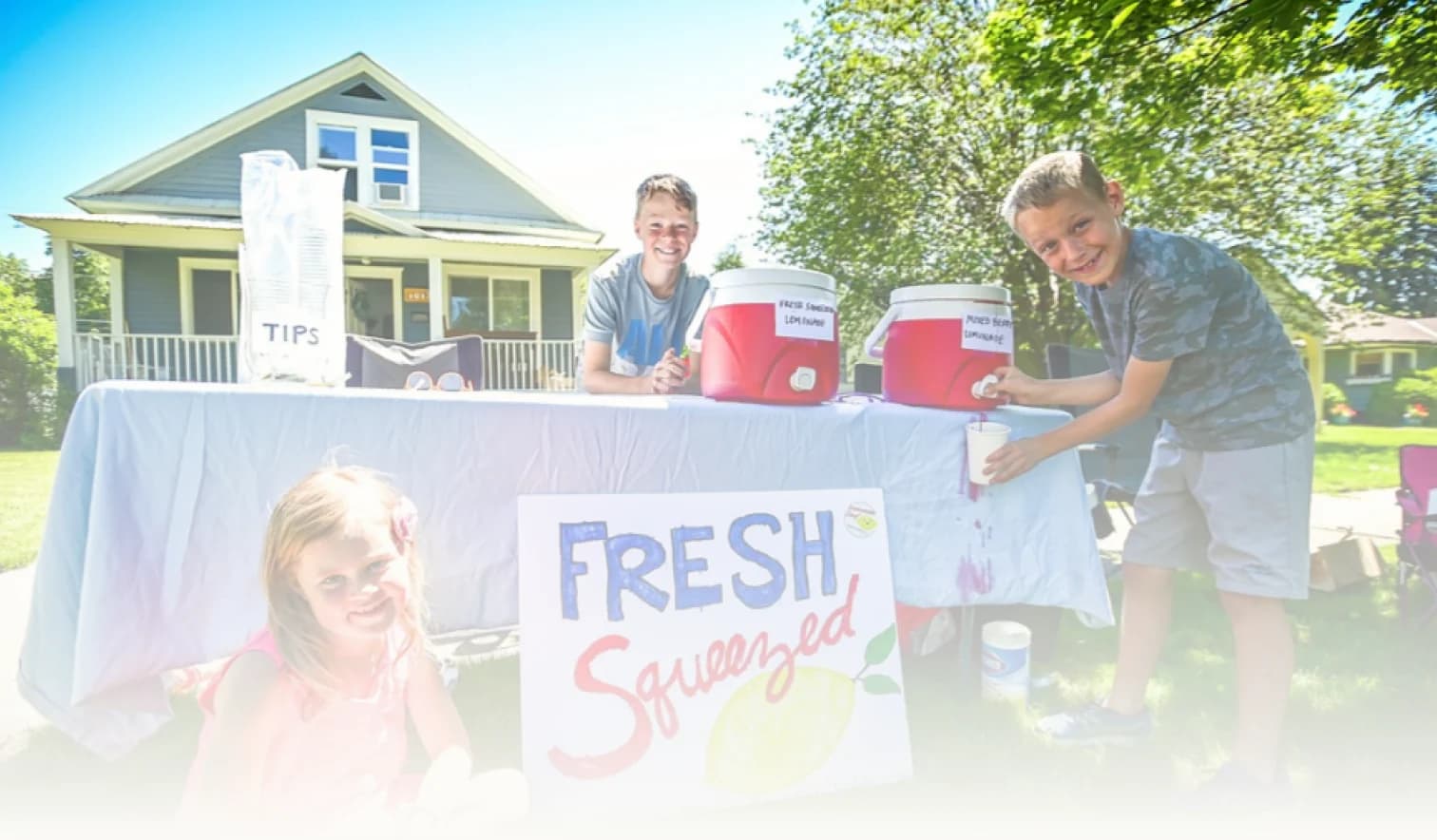 Two kids pouring lemonade under a hand-painted Fresh Squeezed sign